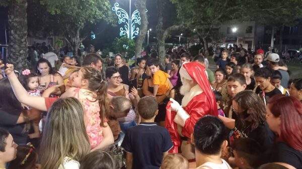 A imagem contem um pessoa vestida de papai Noel rodeada de crianças