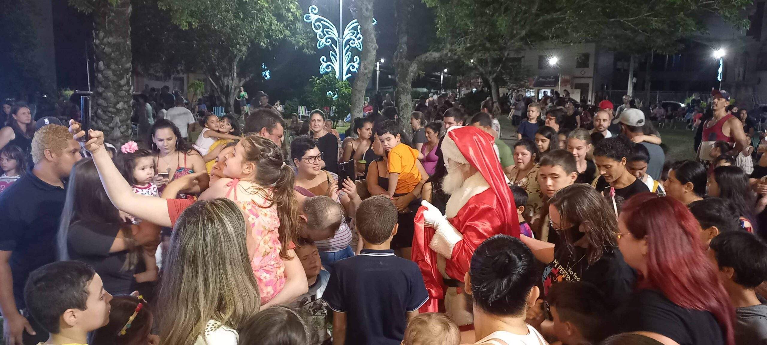A imagem contem um pessoa vestida de papai Noel rodeada de crianças