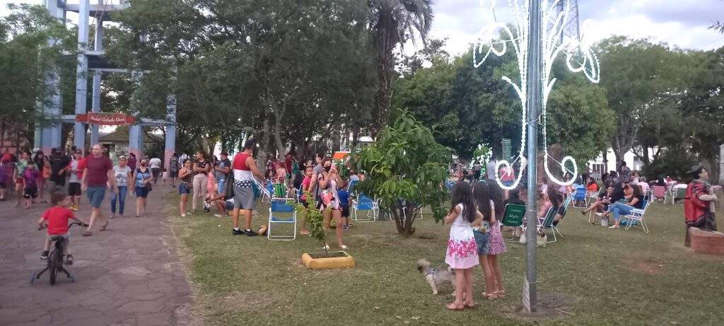 A imagem contem crianças na praca comemorando o Natal